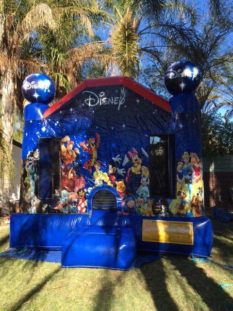 A blue Disney-themed inflatable bounce house with various cartoon characters on the front, set outdoors on grass.