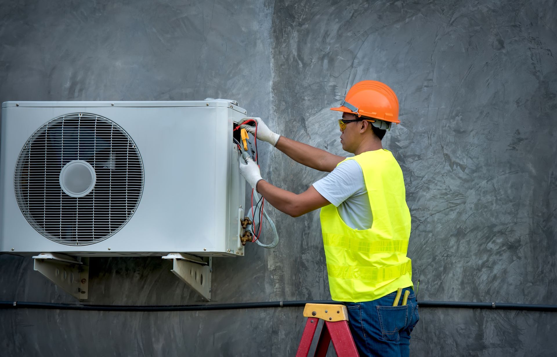 Action Heating And Cooling is standing on a ladder fixing an air conditioner.