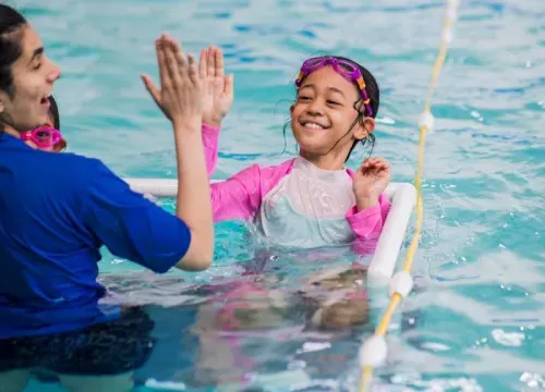 A woman is giving a child a high five in a swimming pool.