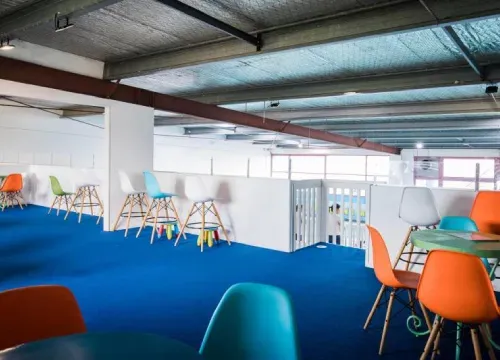 A room with blue carpet and colorful chairs and tables.