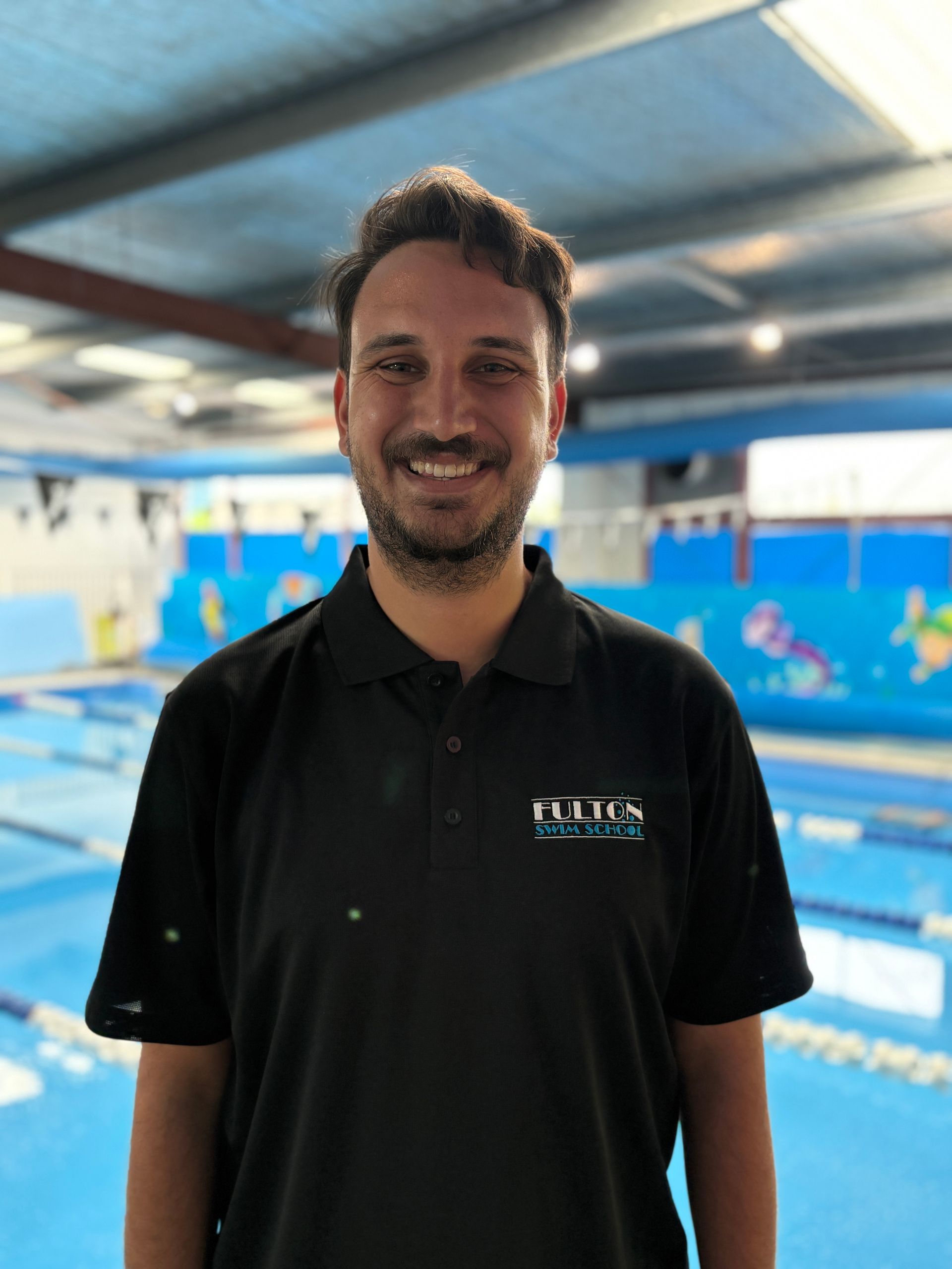 A man with a beard is wearing a blue jacket and smiling for the camera.