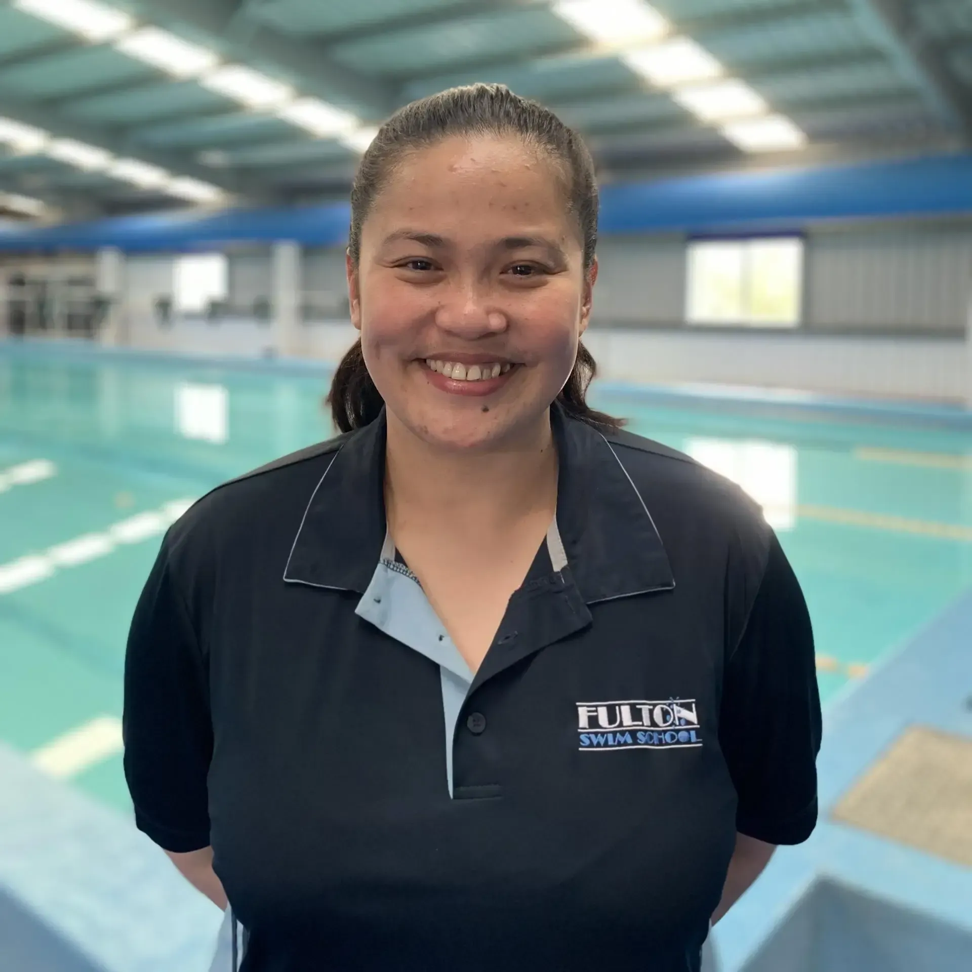 A woman is smiling in front of a swimming pool.