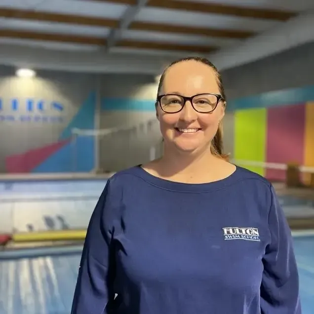 A woman is smiling in front of a swimming pool.