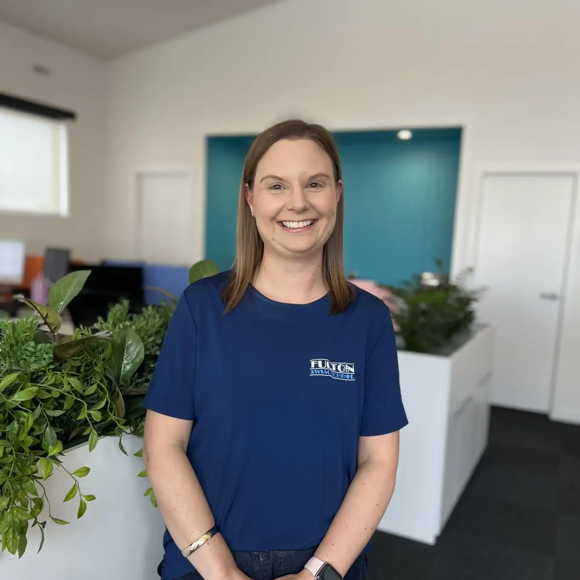 A woman in a blue shirt is smiling in an office.