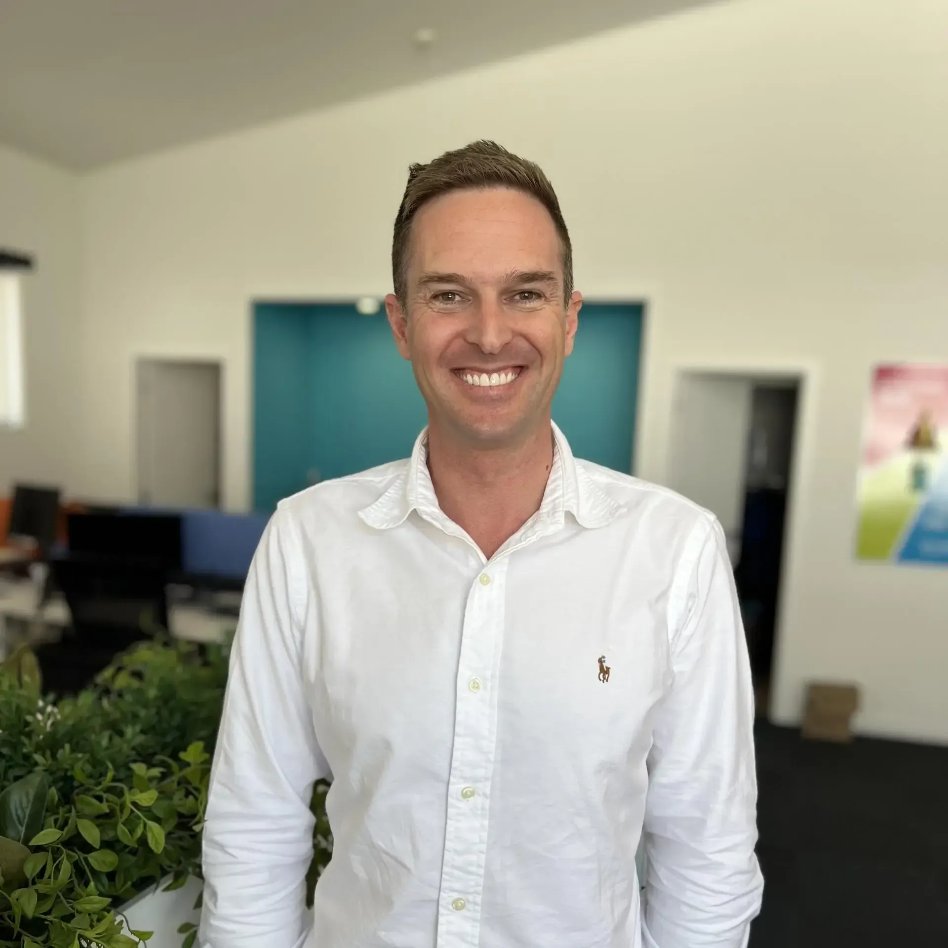 A man in a white shirt is smiling for the camera in an office.