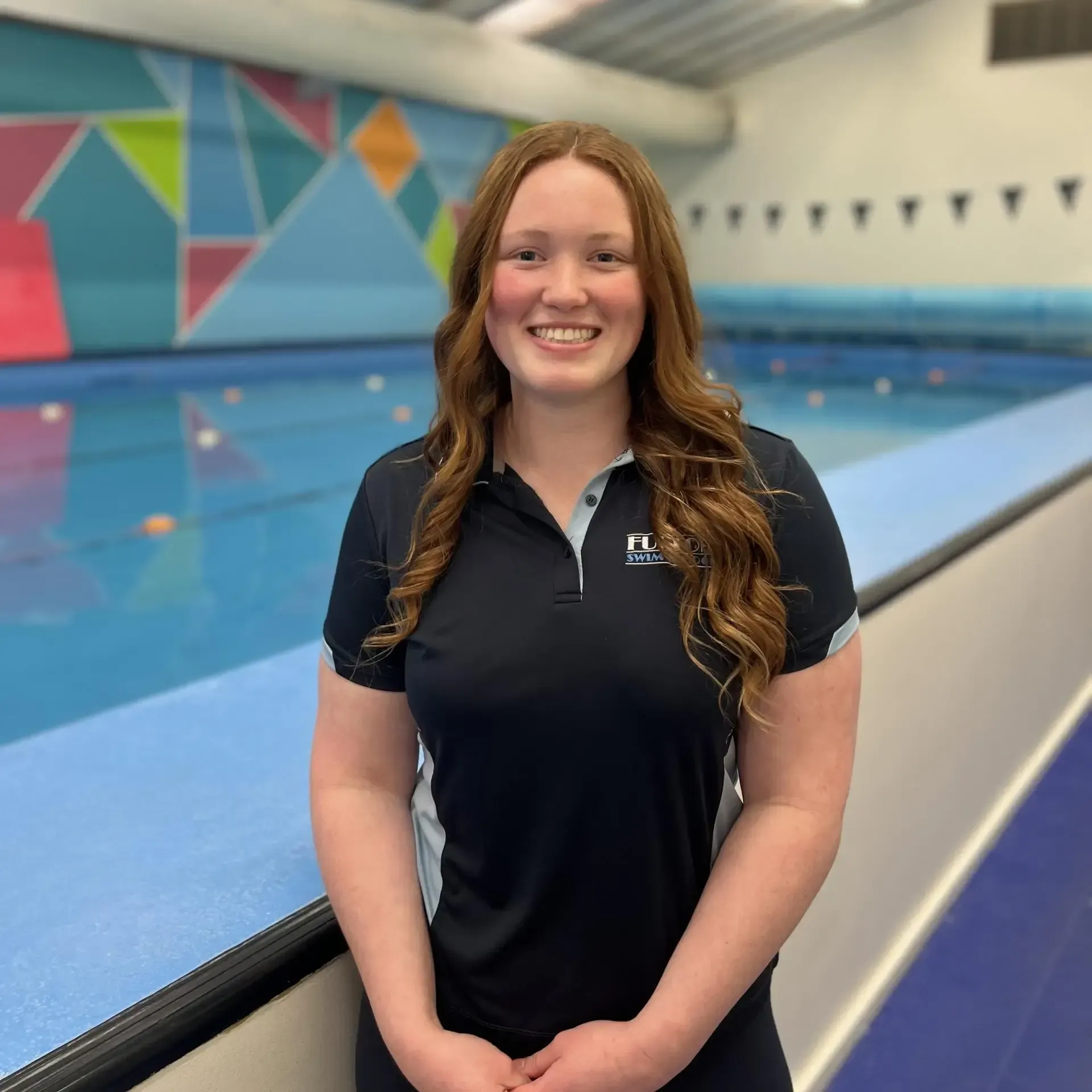 A woman in a black shirt is standing in front of a swimming pool