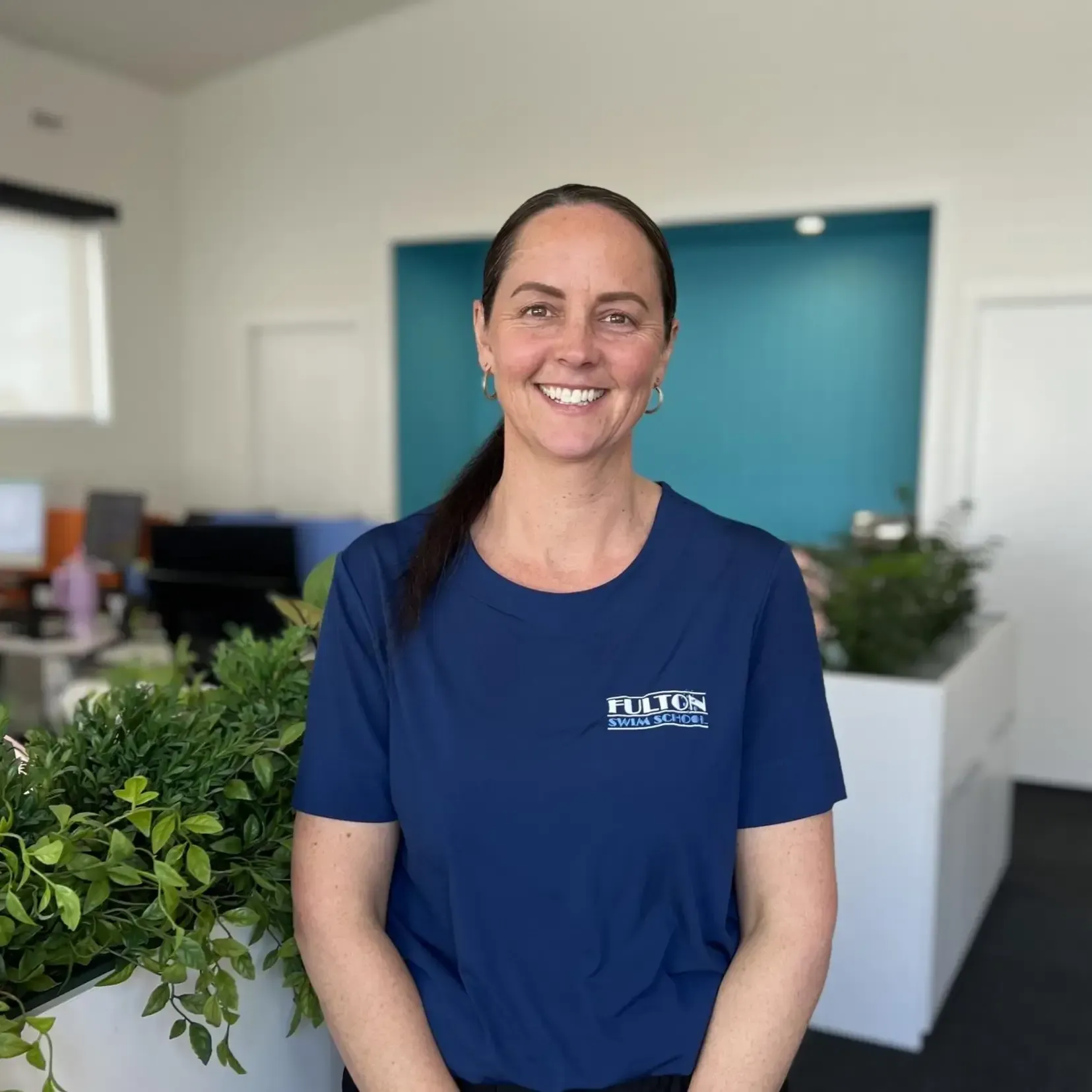 A woman in a blue shirt is smiling in a room.