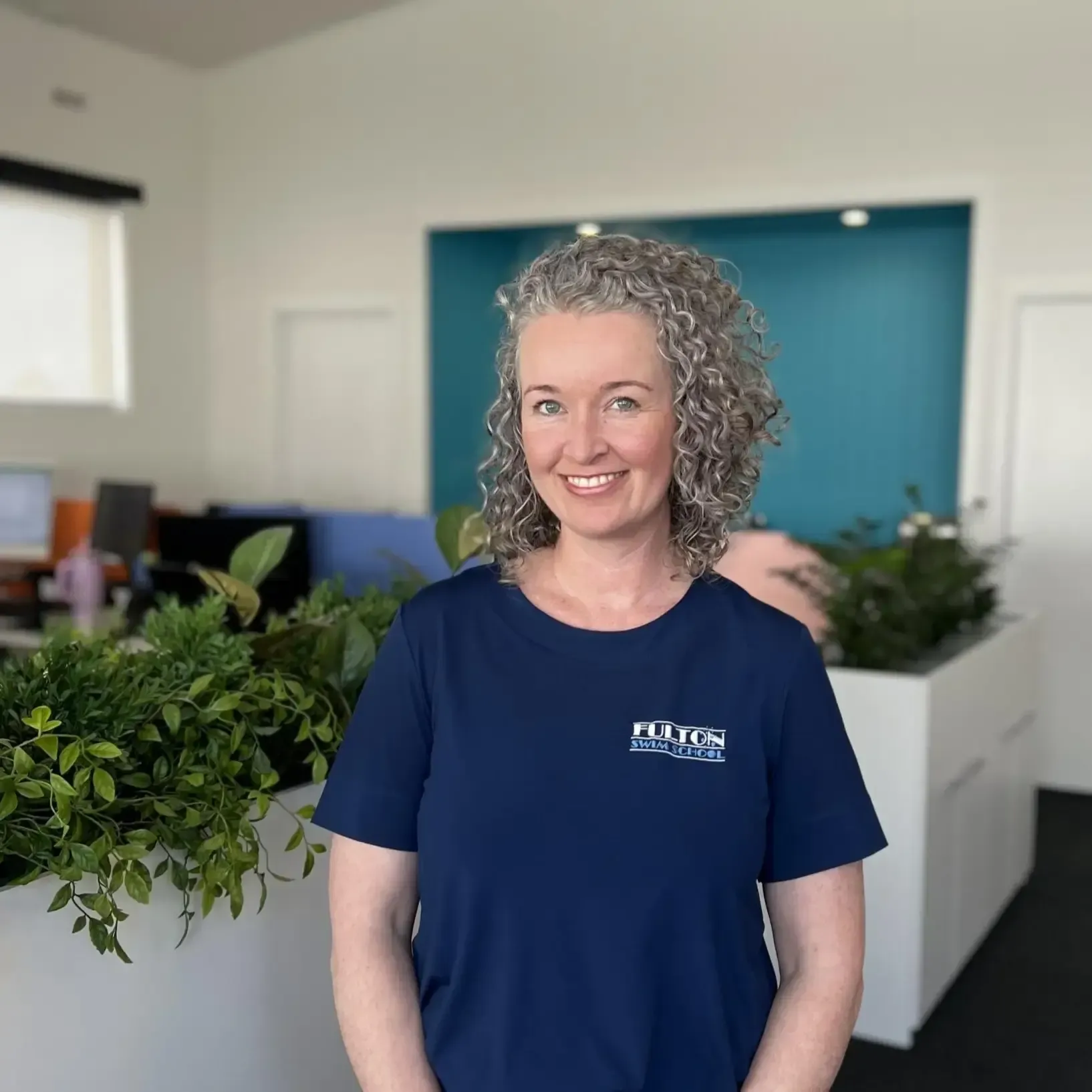 A woman in a blue shirt is standing in front of a potted plant.