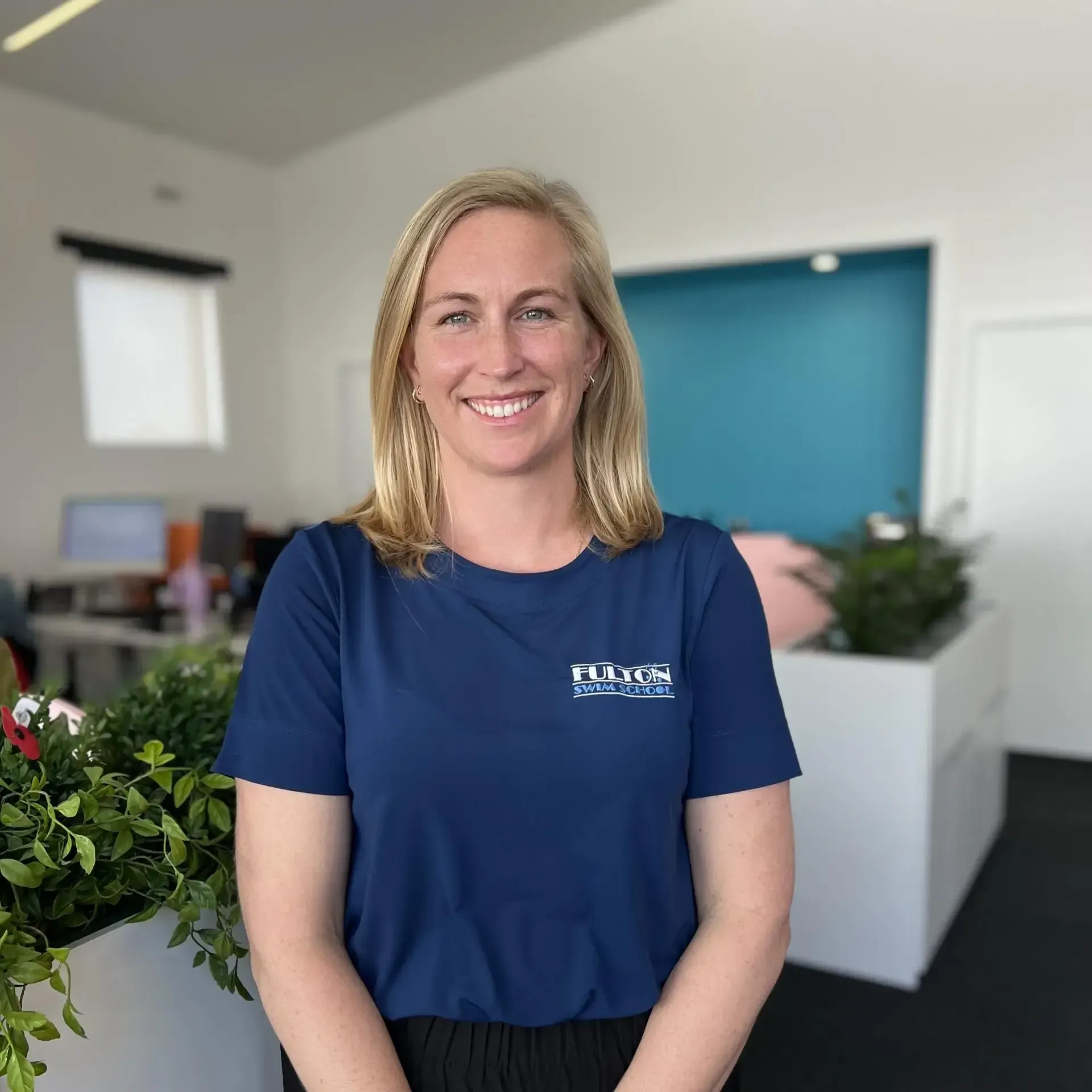 A woman in a blue shirt is smiling in an office.