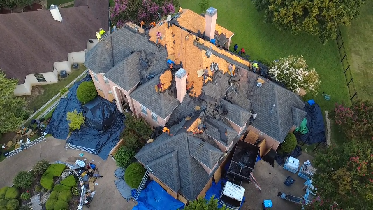 Aerial view of a home with roof damage and repair in progress; blue tarps cover areas.
