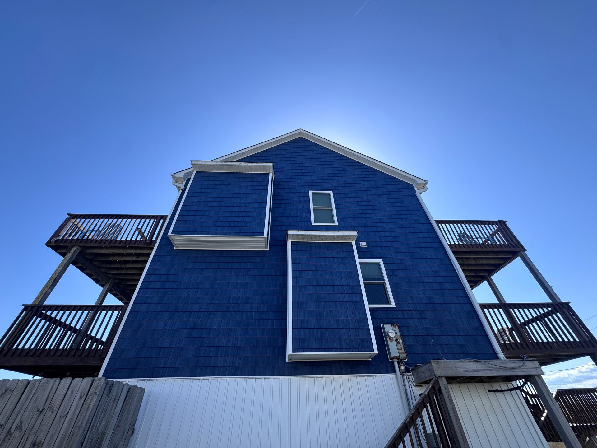 Blue house with white trim and balconies against a bright blue sky.