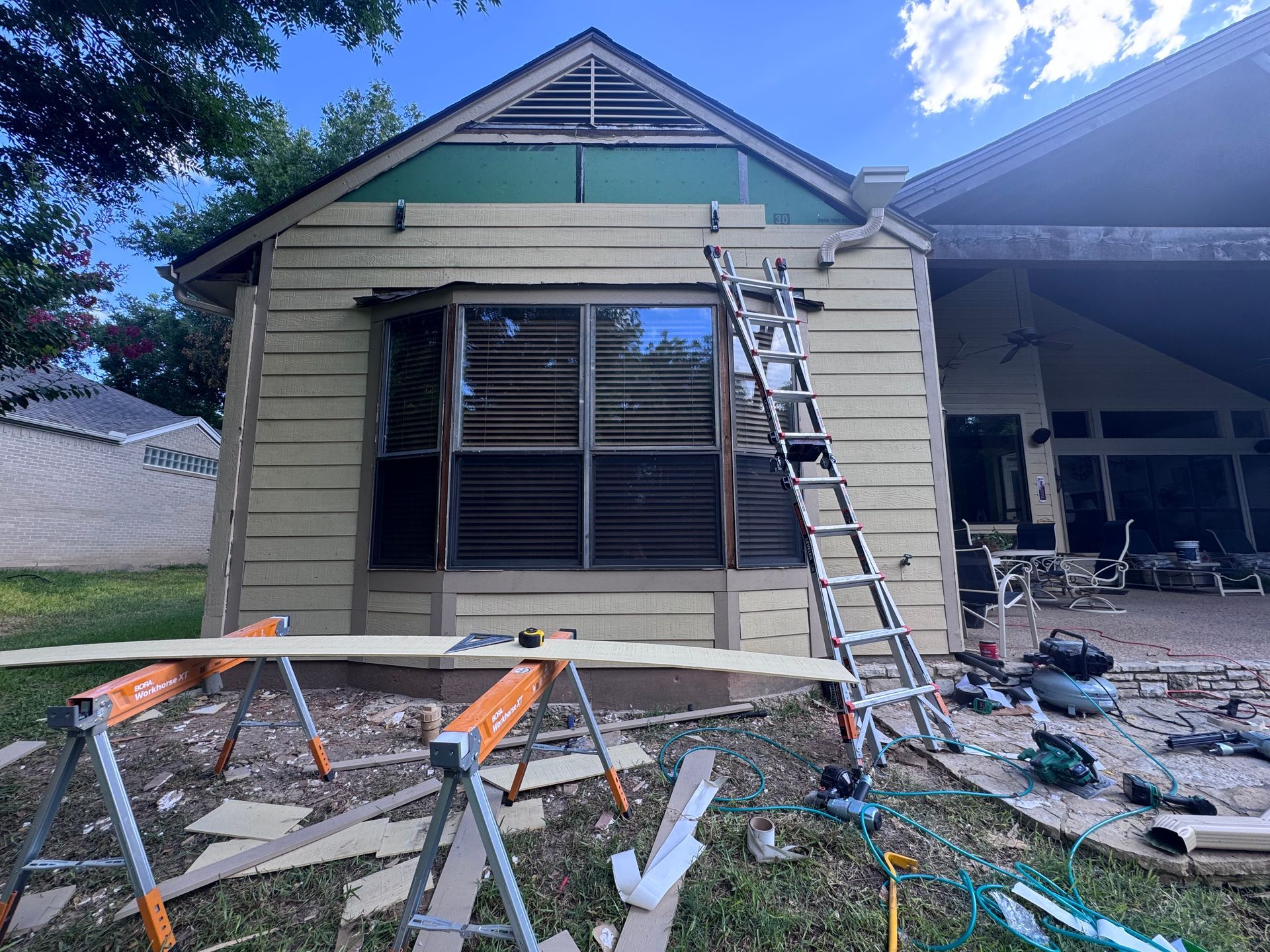 House exterior under construction; ladder, saw horses, tools, and materials.