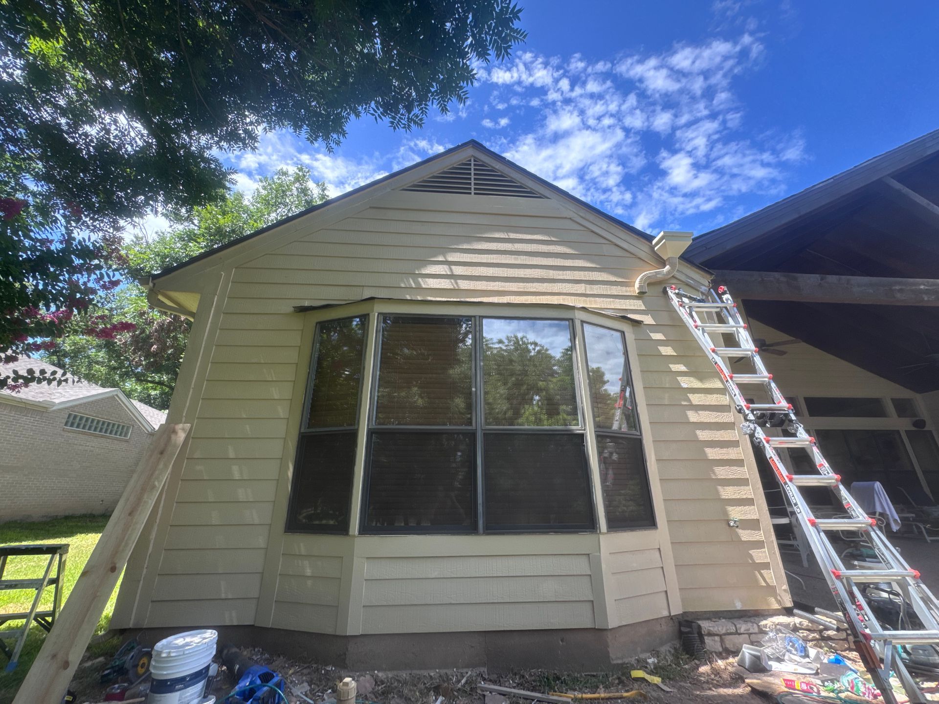 House exterior with tan siding and large bay window; ladder on the side.