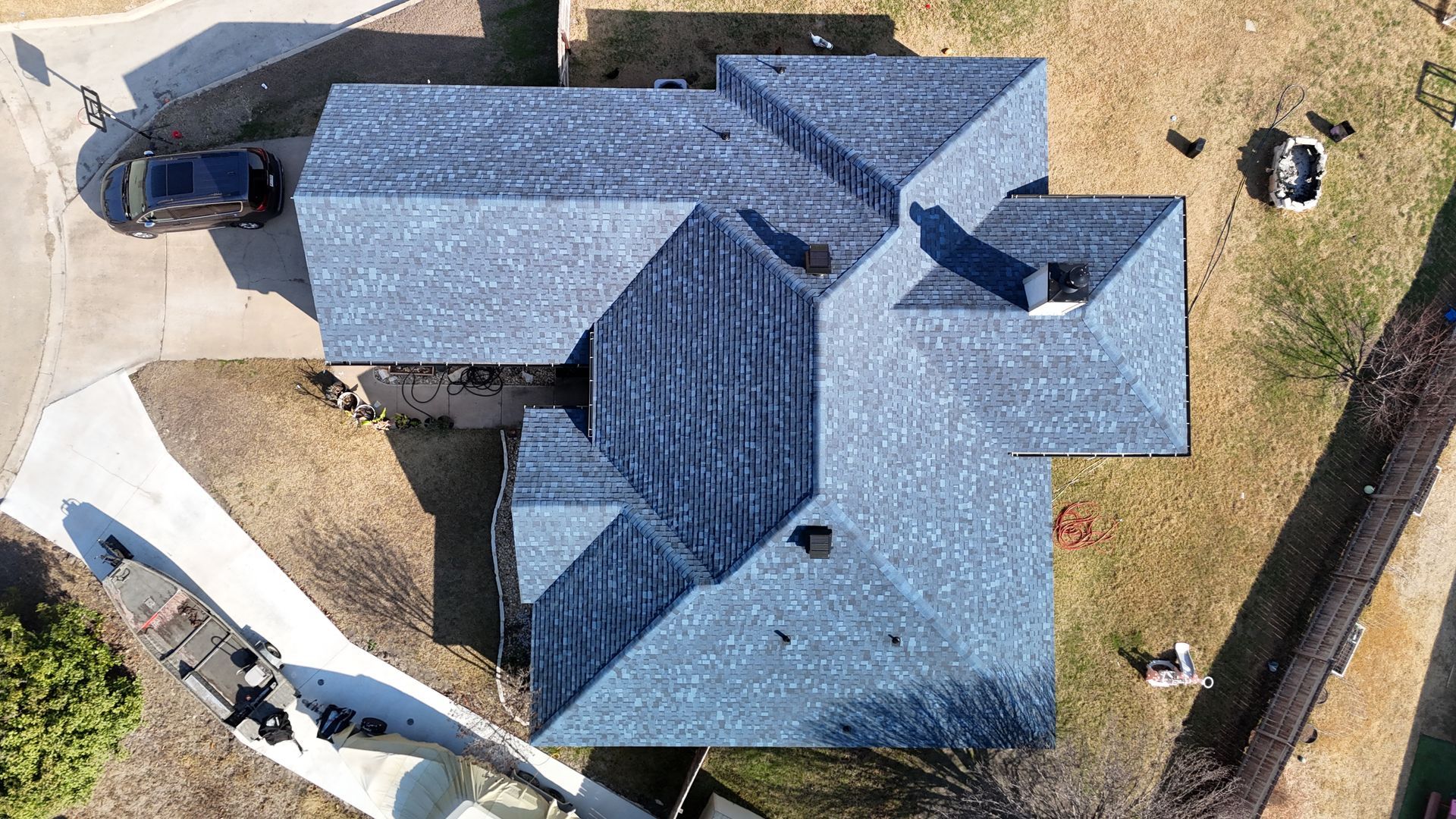 Overhead view of a house with a complex blue shingle roof. A car sits in the driveway, and a lawn surrounds it.