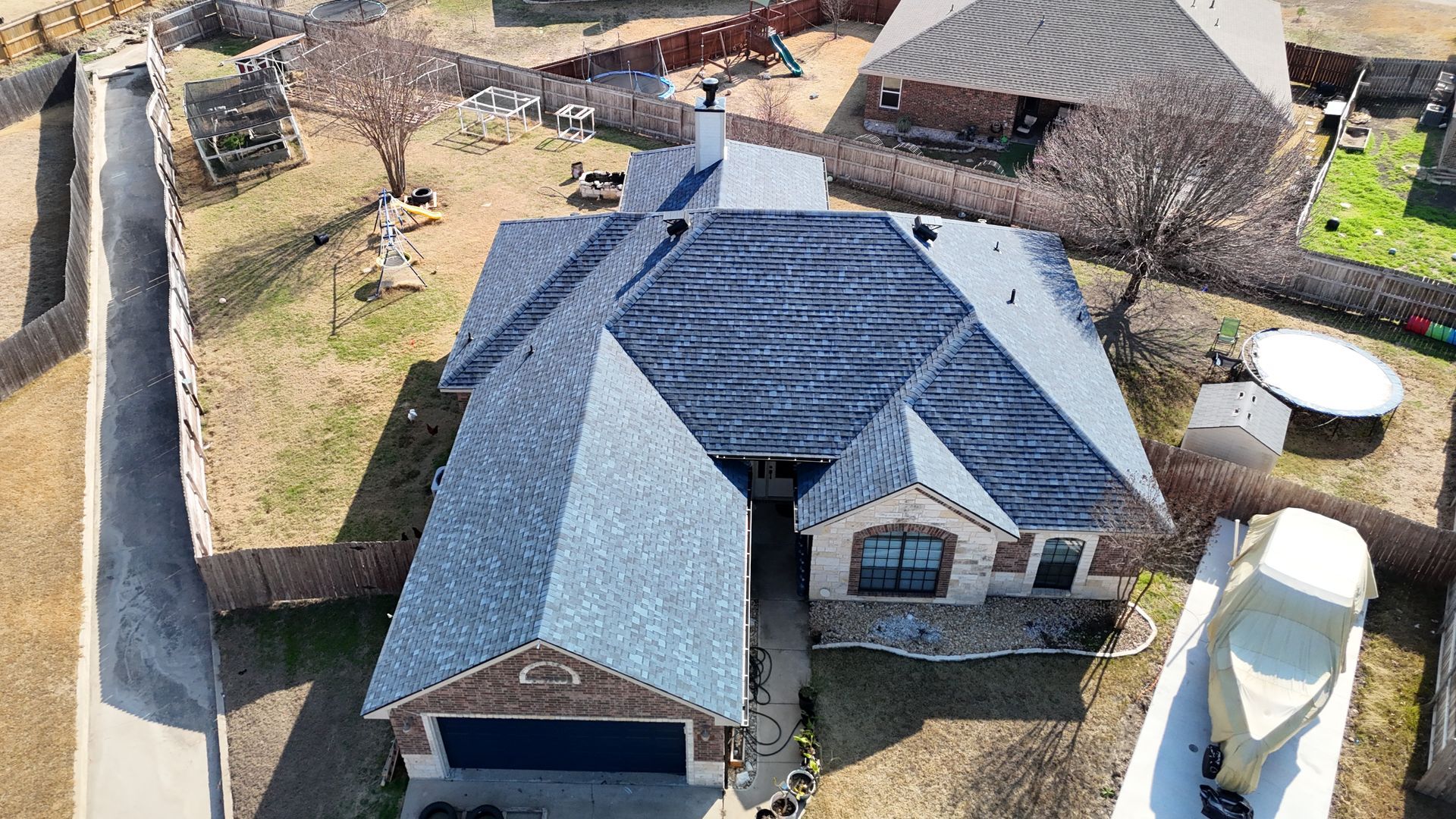 Aerial view of a house with a dark blue roof, a detached boat, and a brown fence.