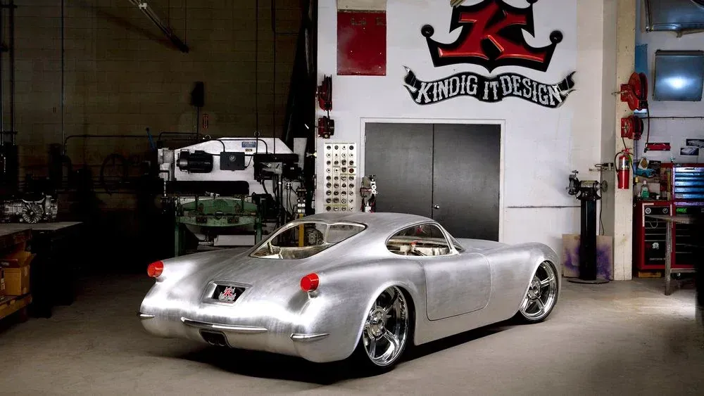 A silver car is parked in a garage in front of a sign that says Kindig it Design