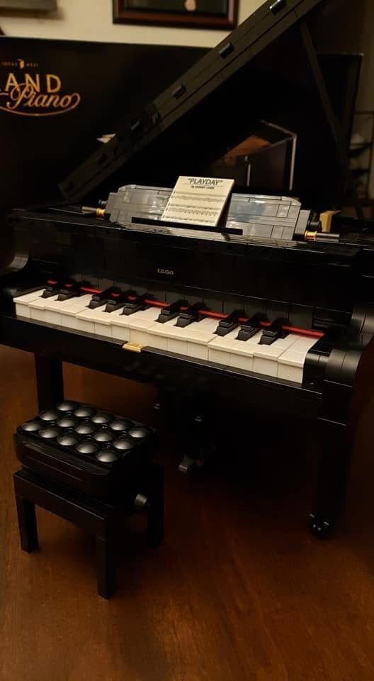 A black grand piano is sitting on a wooden floor next to a stool.
