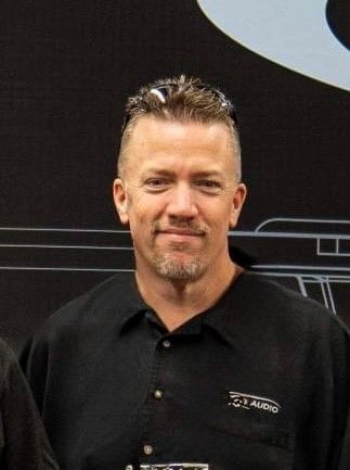 A man with a beard is wearing a black shirt and sunglasses.