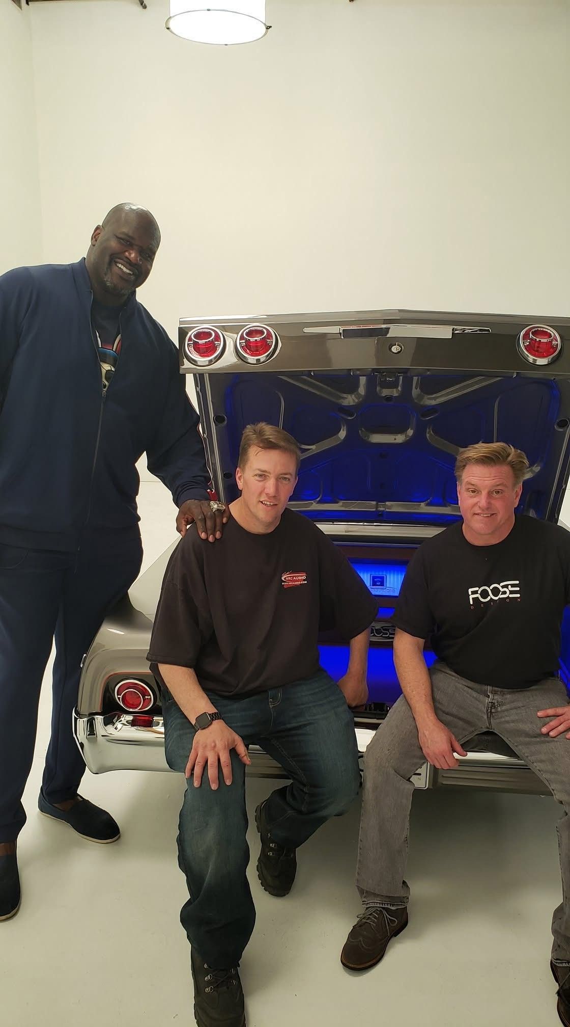 Three men are posing for a picture in front of a car.