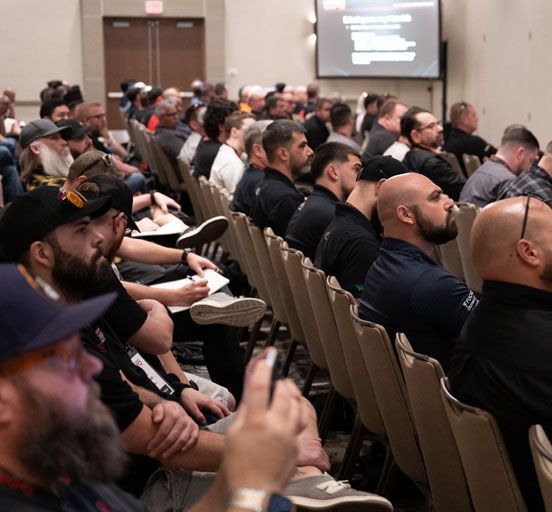 Audience in a conference room listening to a presentation. People are taking notes.