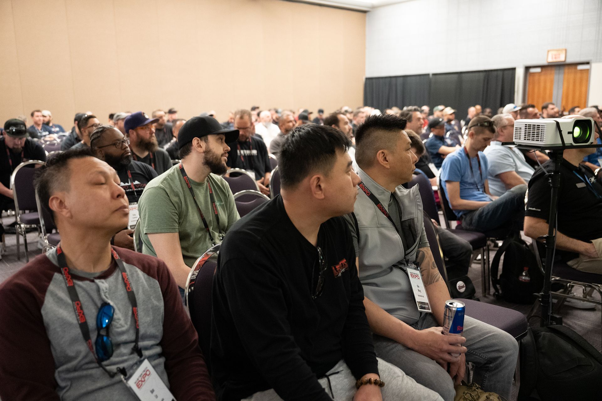 Audience in a conference room; people listen to a presentation. Many have neutral expressions.