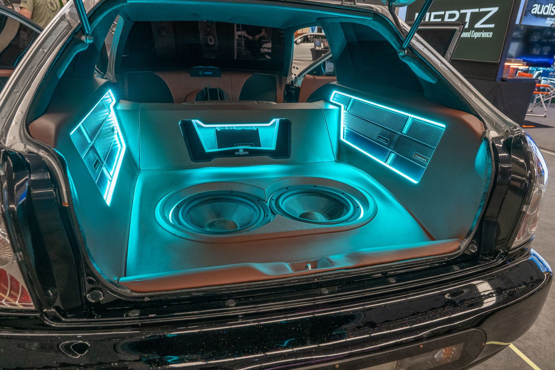 Car trunk with custom audio setup. Blue LED lighting illuminates speakers, amps, and trim.