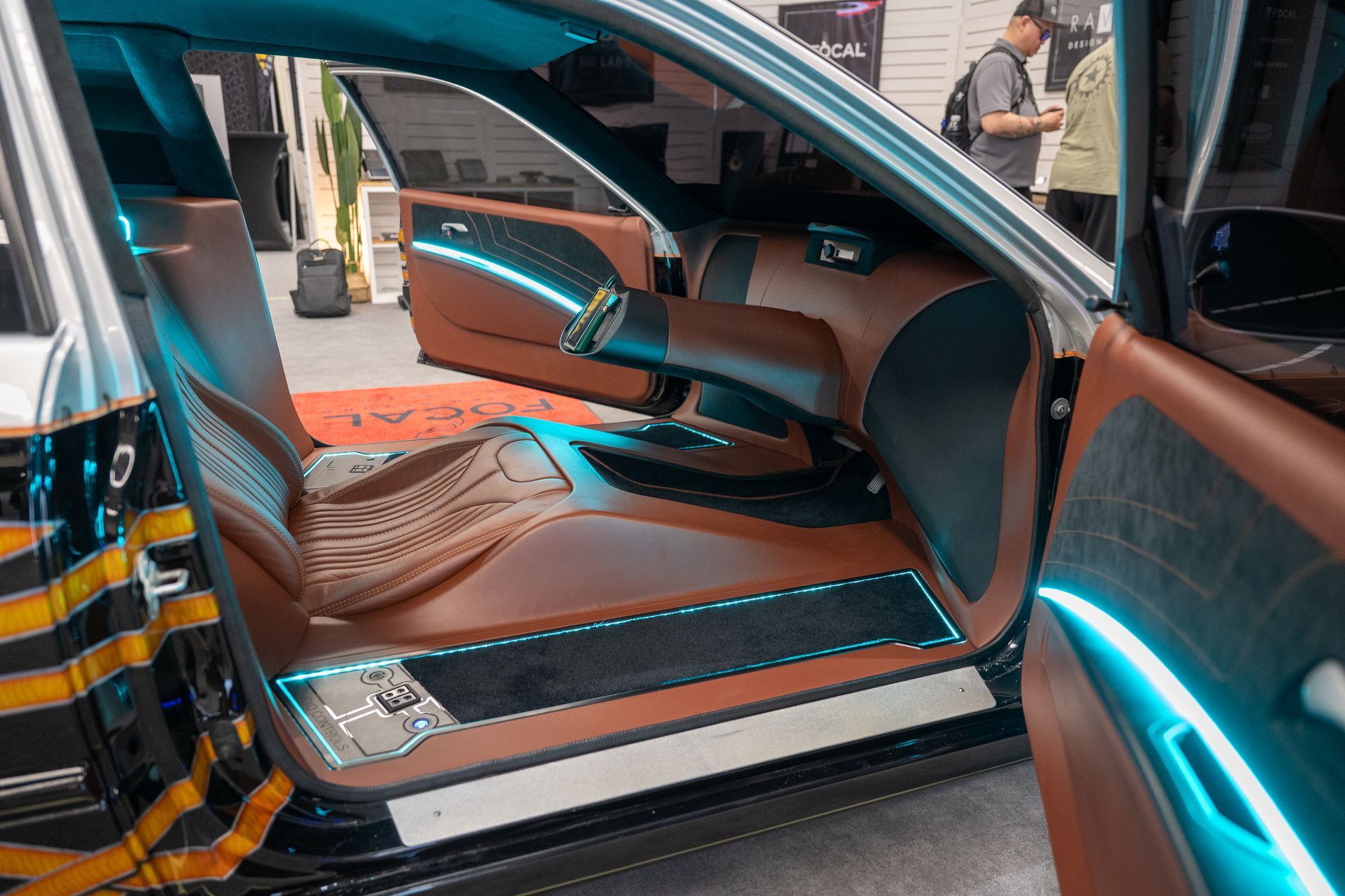 Brown leather car interior with blue LED lights. Open door, showing seats and trim. People in background.