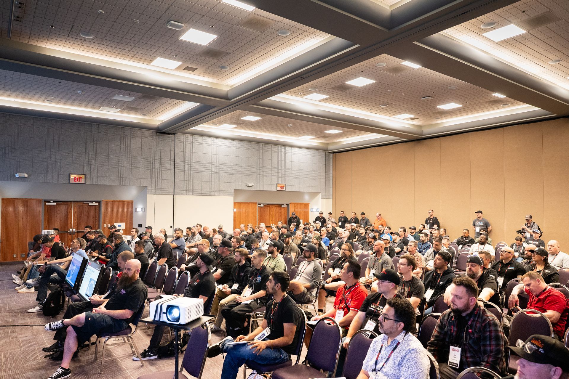 Audience in a large conference room, watching a presentation on a projector screen.