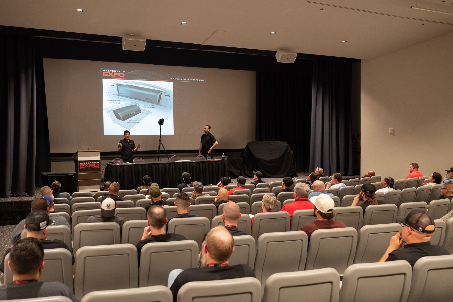 Audience seated, watching presentation on screen. Two men stand at the podium.