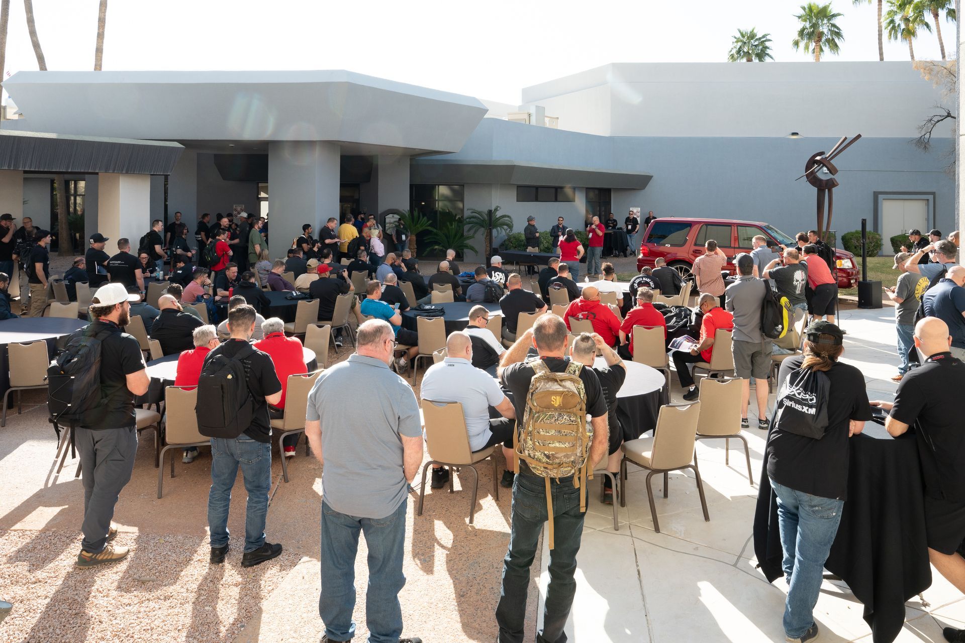 People gathered outdoors at tables in front of a building; some are wearing red.