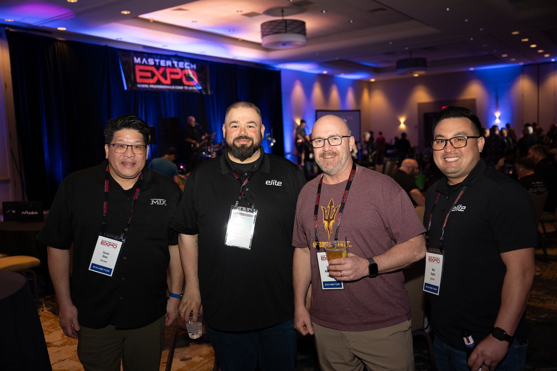Four men smiling, at an event. The backdrop is a stage with an 