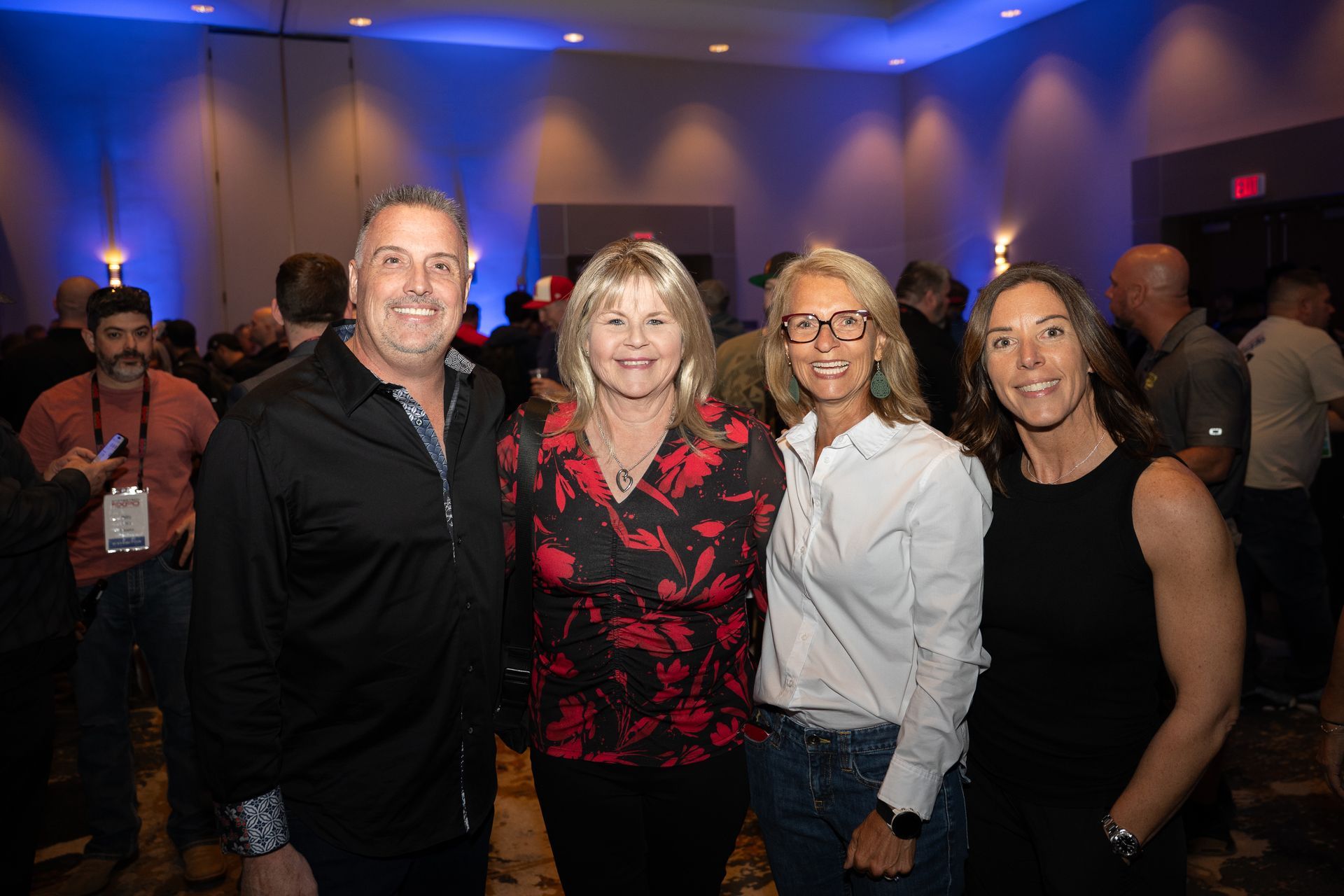 Four people smiling at a conference. Two women and two men pose for a photo in a room with a crowd.