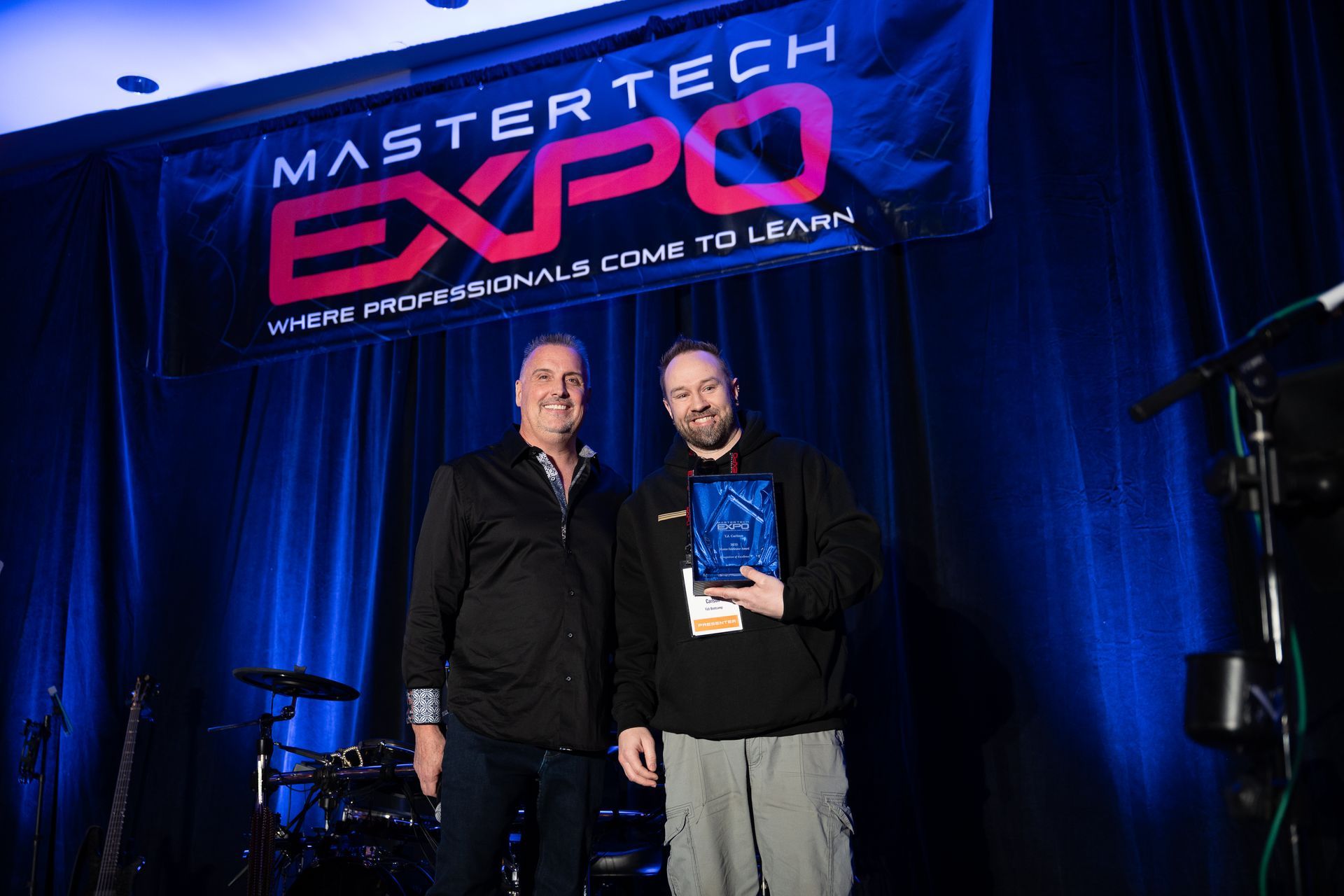 Two men on a stage with a banner that reads 