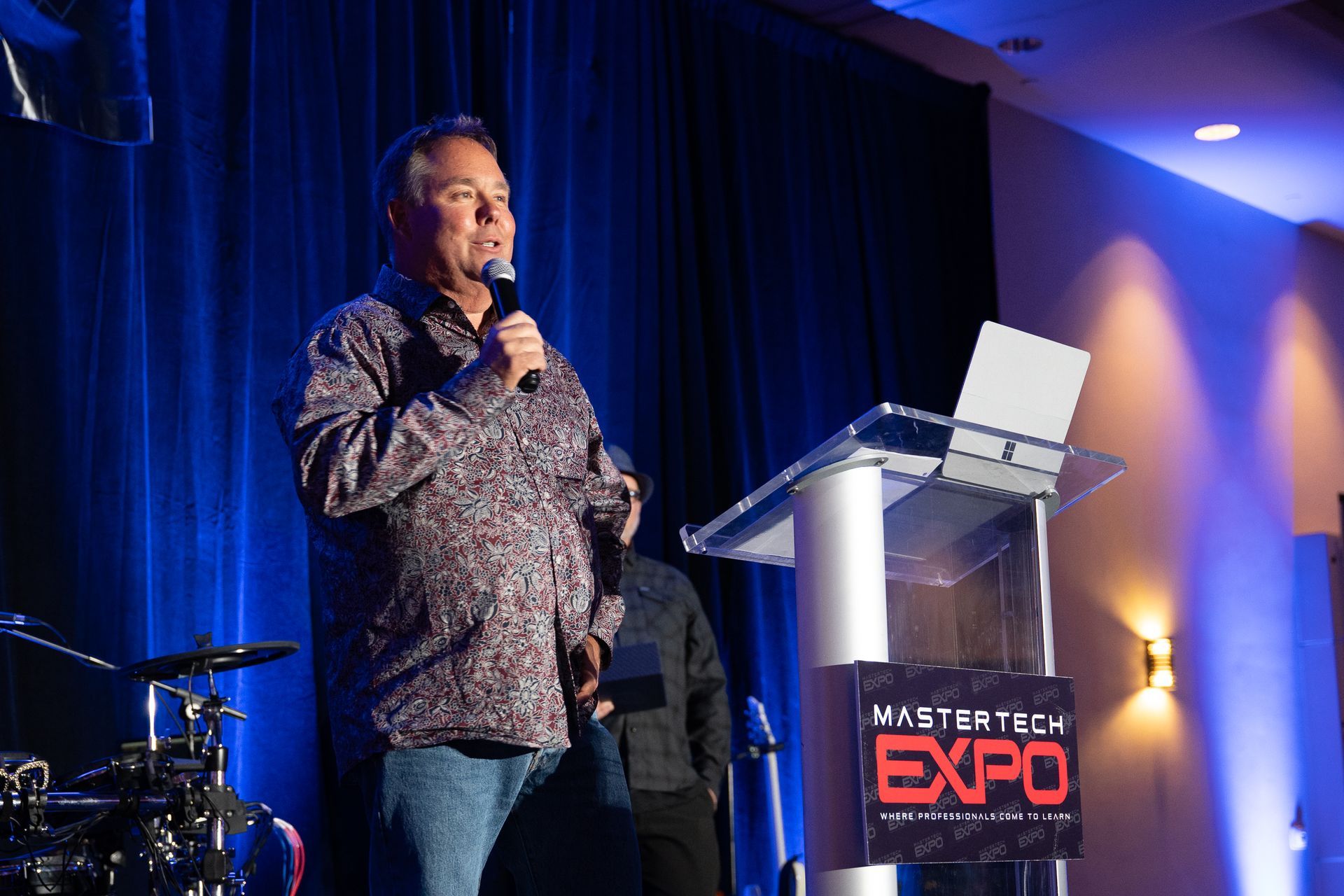 Man speaking at a podium with a laptop, at the Master Tech Expo.