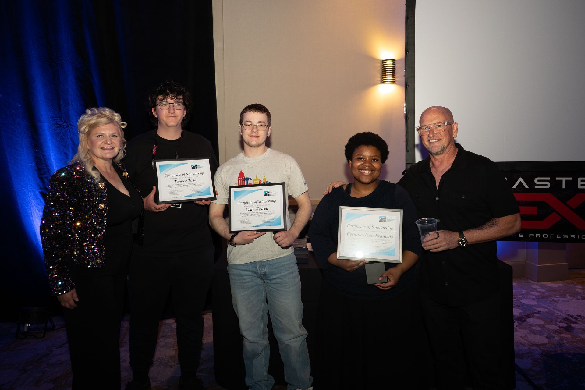 People holding certificates, smiling, posing together on a stage.