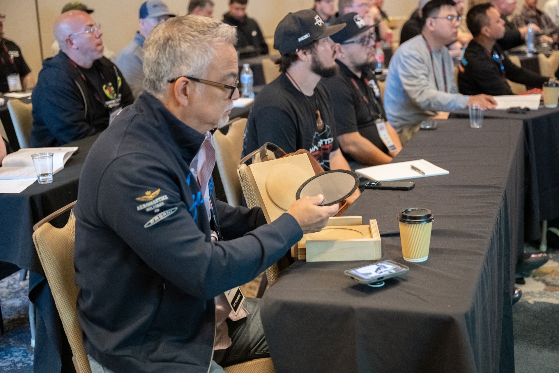 Man examining a circular object during a conference, attendees seated at tables.