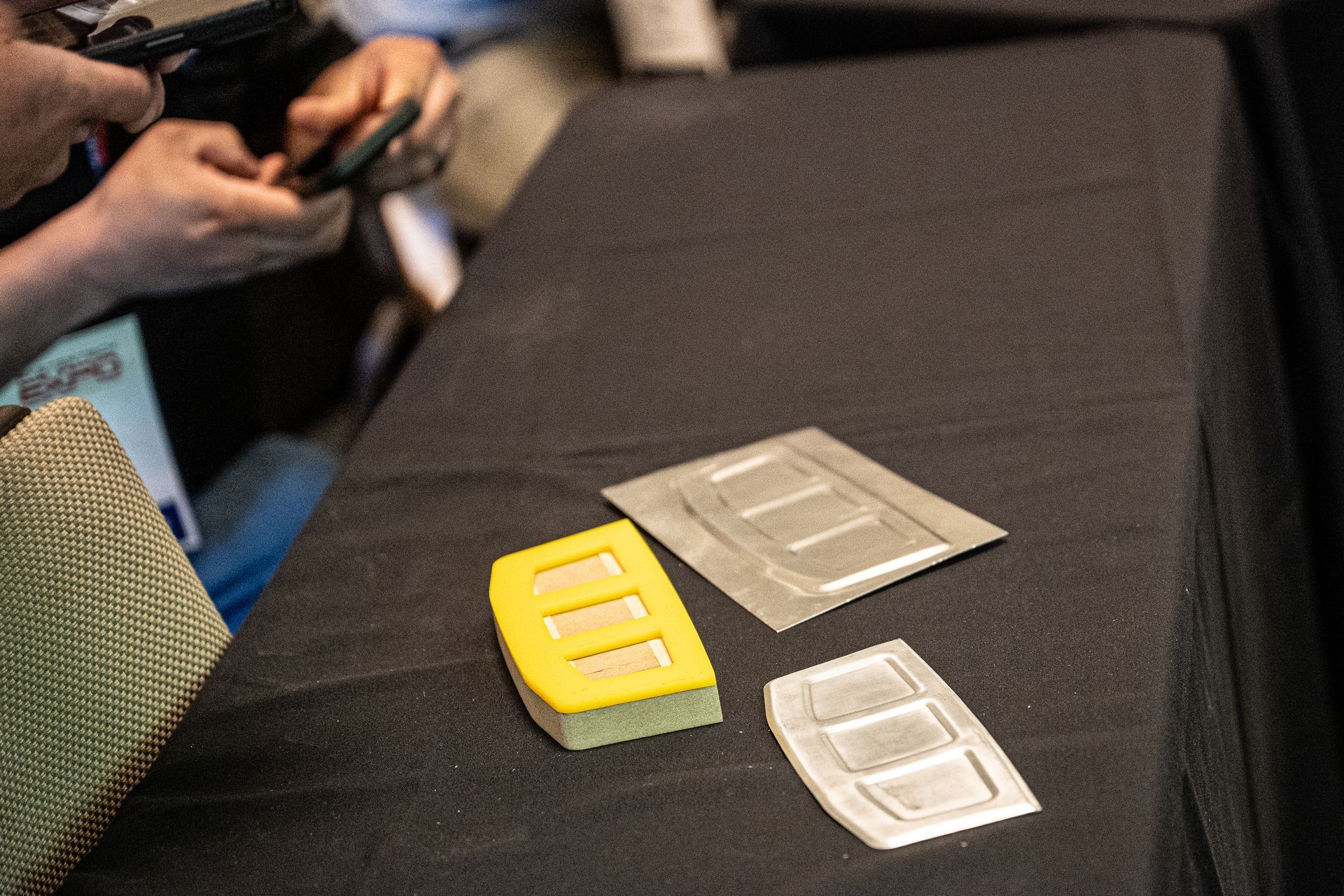 Three rectangular objects, two silver and one yellow, with slotted designs on a black surface.