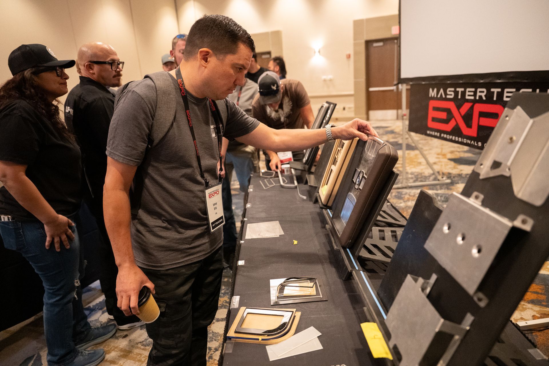 People examine mechanical parts at a trade show. A man points to a display, others look on.