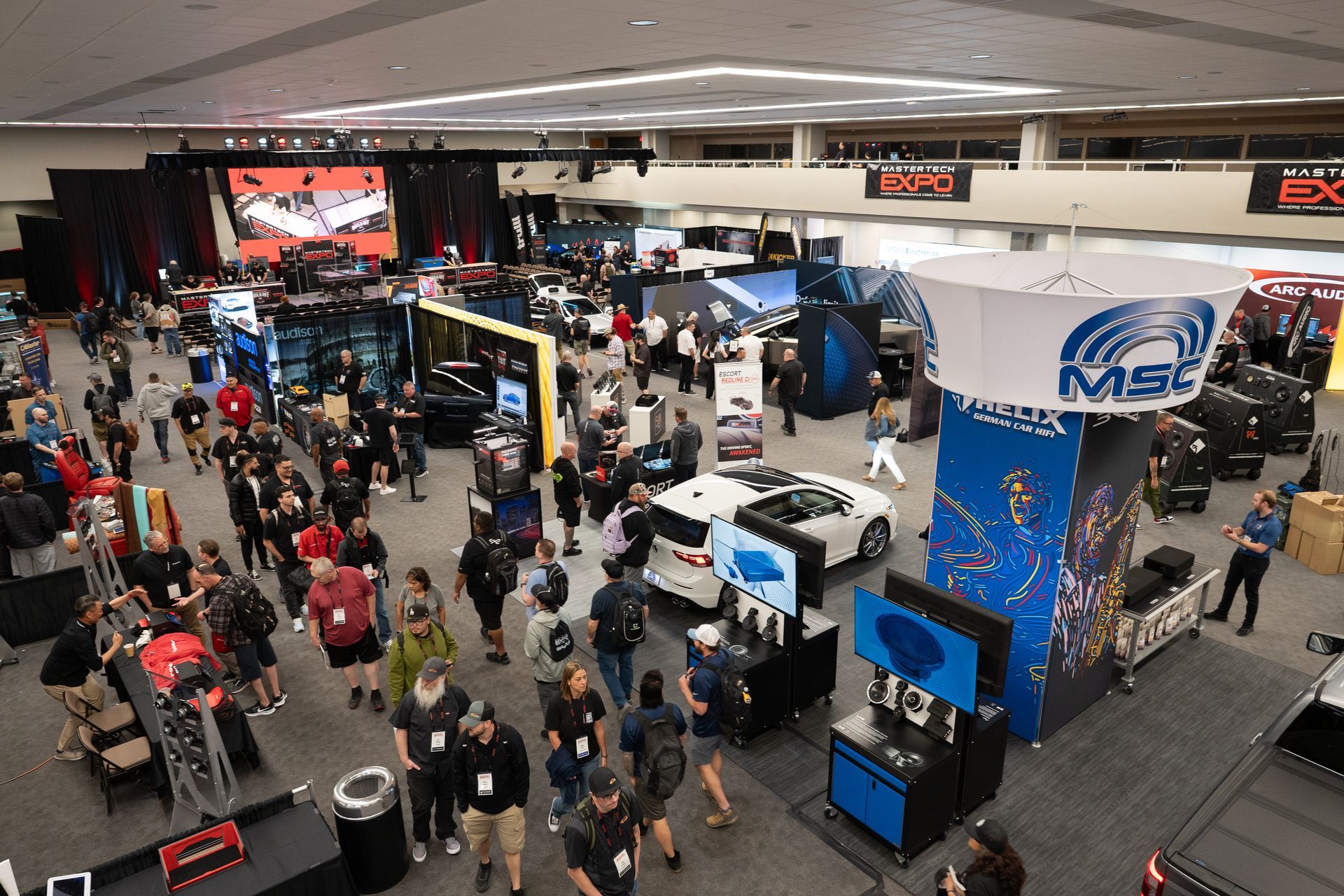 Large convention hall filled with people and displays, including cars, signs, and exhibits.