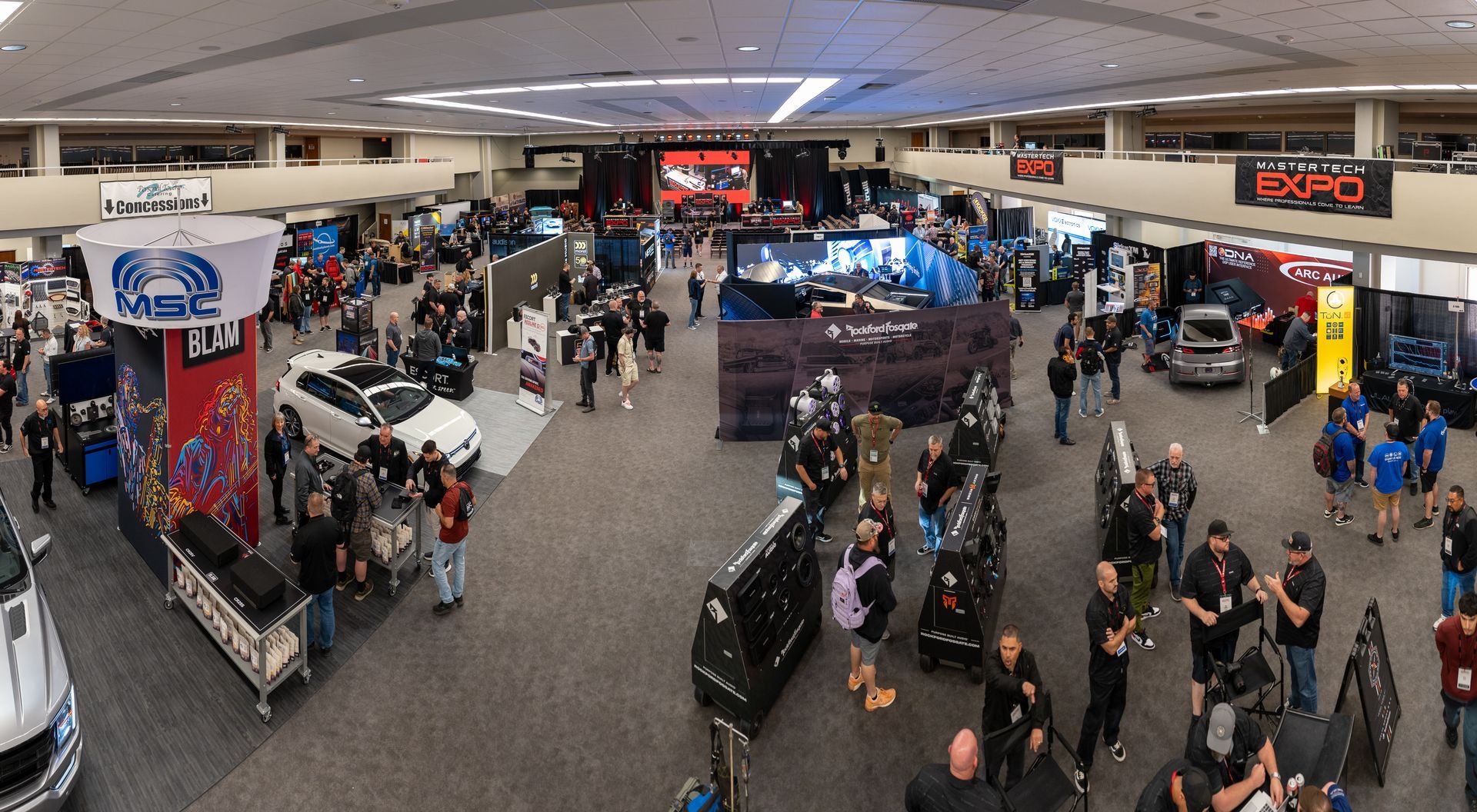 An expansive indoor automotive expo with numerous booths, cars, and attendees; overhead view.