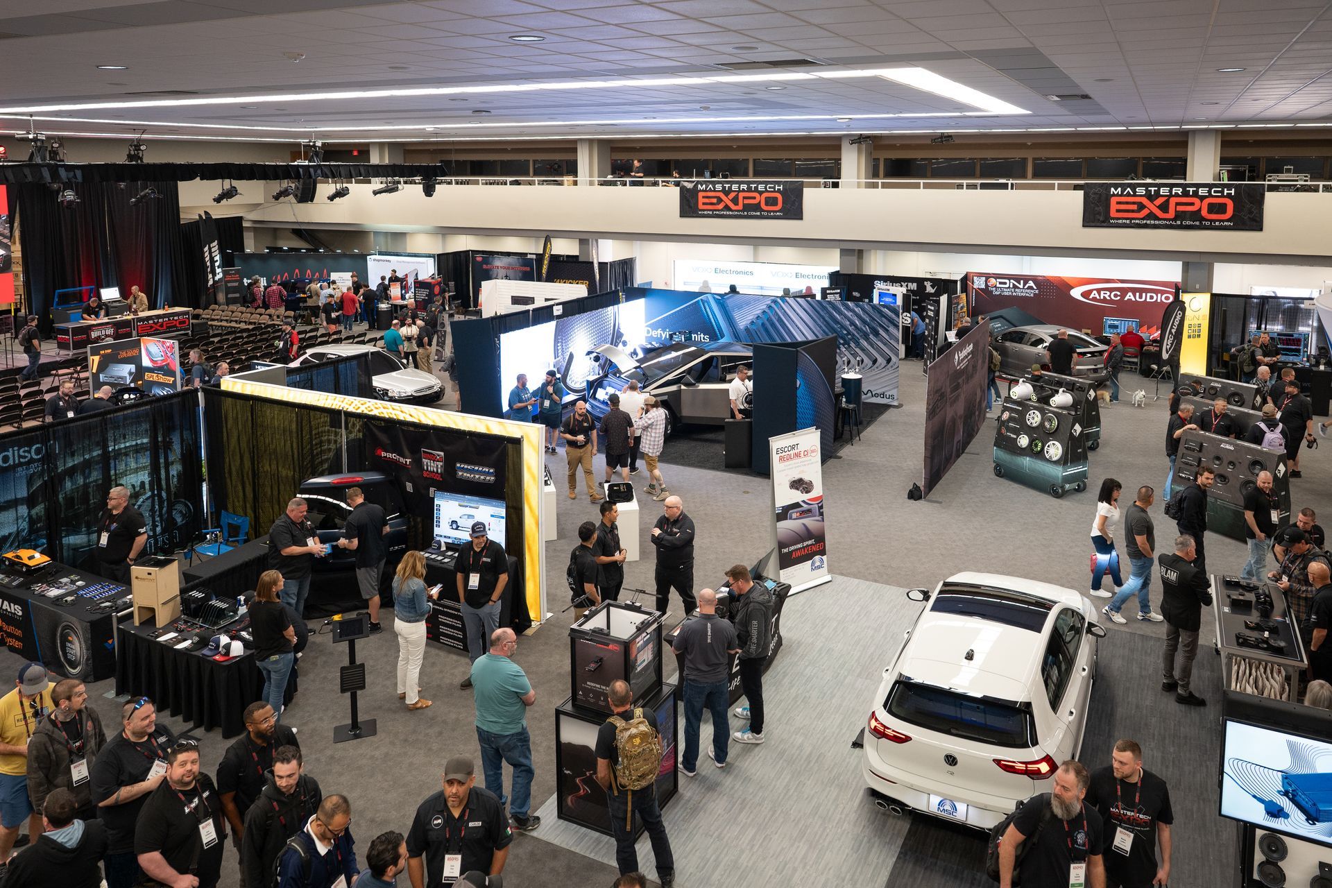Large expo hall with numerous booths, people, and a white car on display.