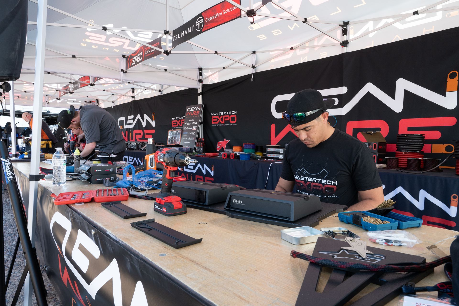 Man at a booth with products on display at an expo. Black, red, and white colors are present.