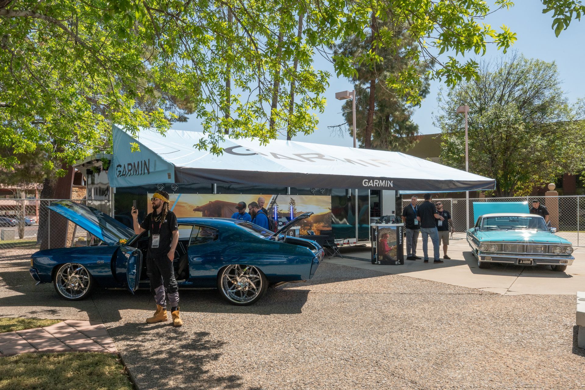 Blue classic cars displayed near a promotional tent; a person stands next to one with the hood open.