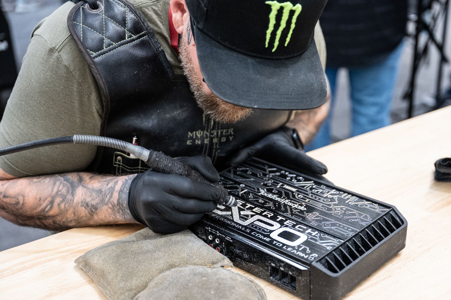Man in black gloves, cap, and vest, etching design onto a black electronic device.