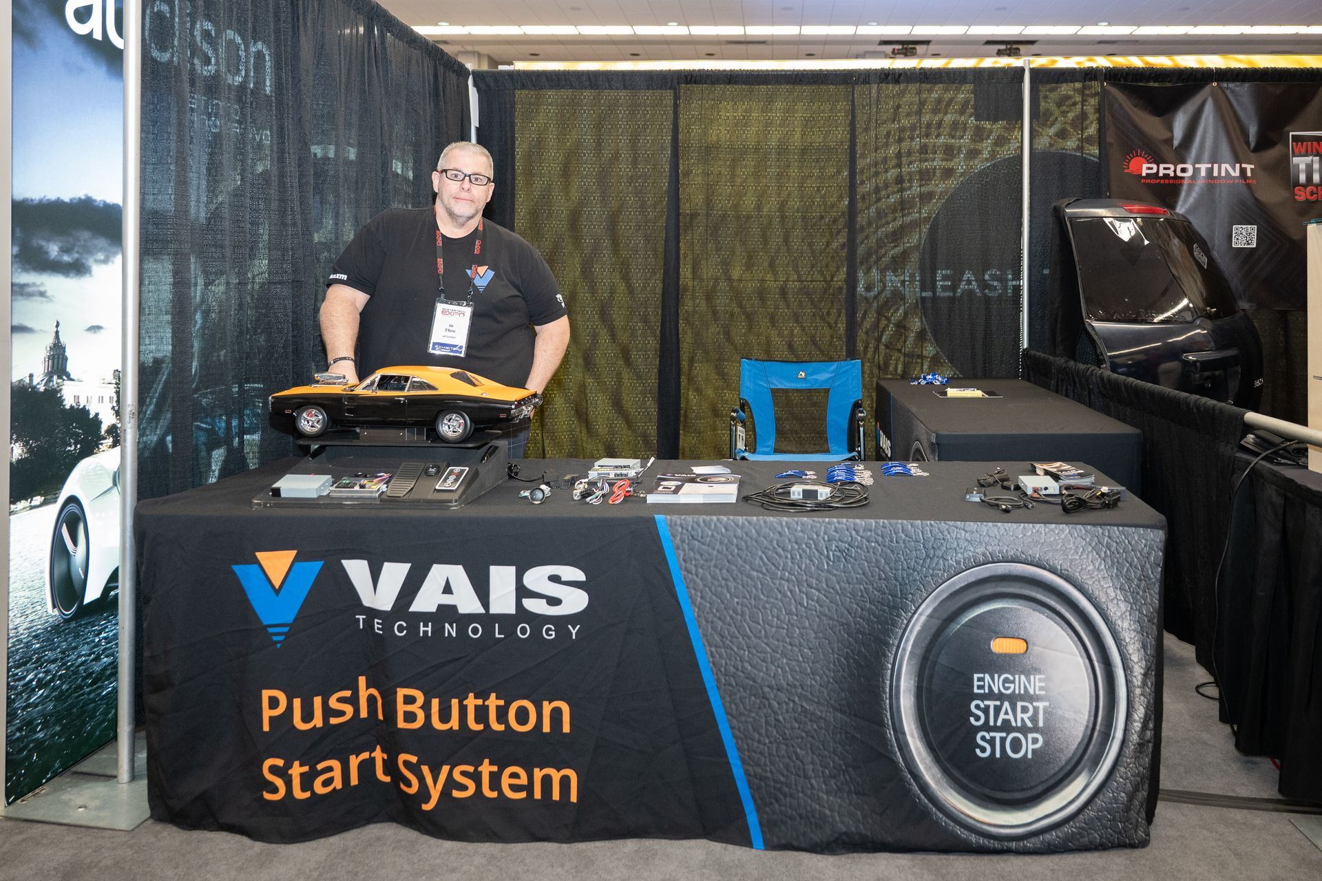 Man at a trade show booth with car part display. VAIS Technologies logo and 
