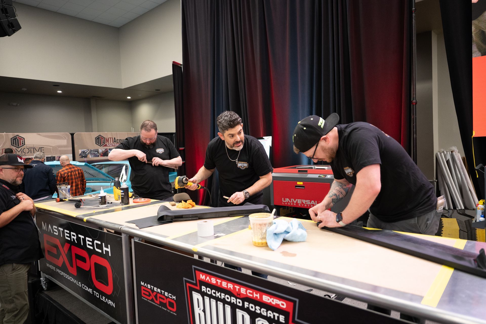 Men working on a car at a trade show booth, installing trim.