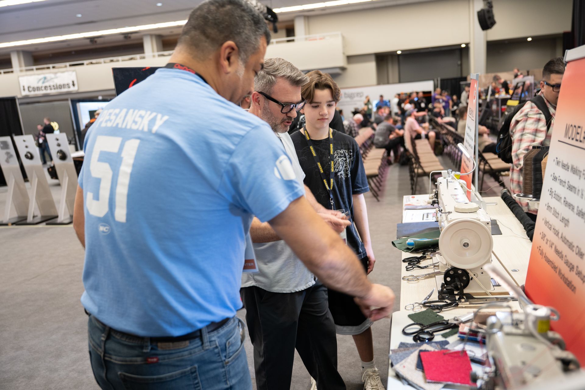 Man in blue shirt, two others examining a display at a convention.