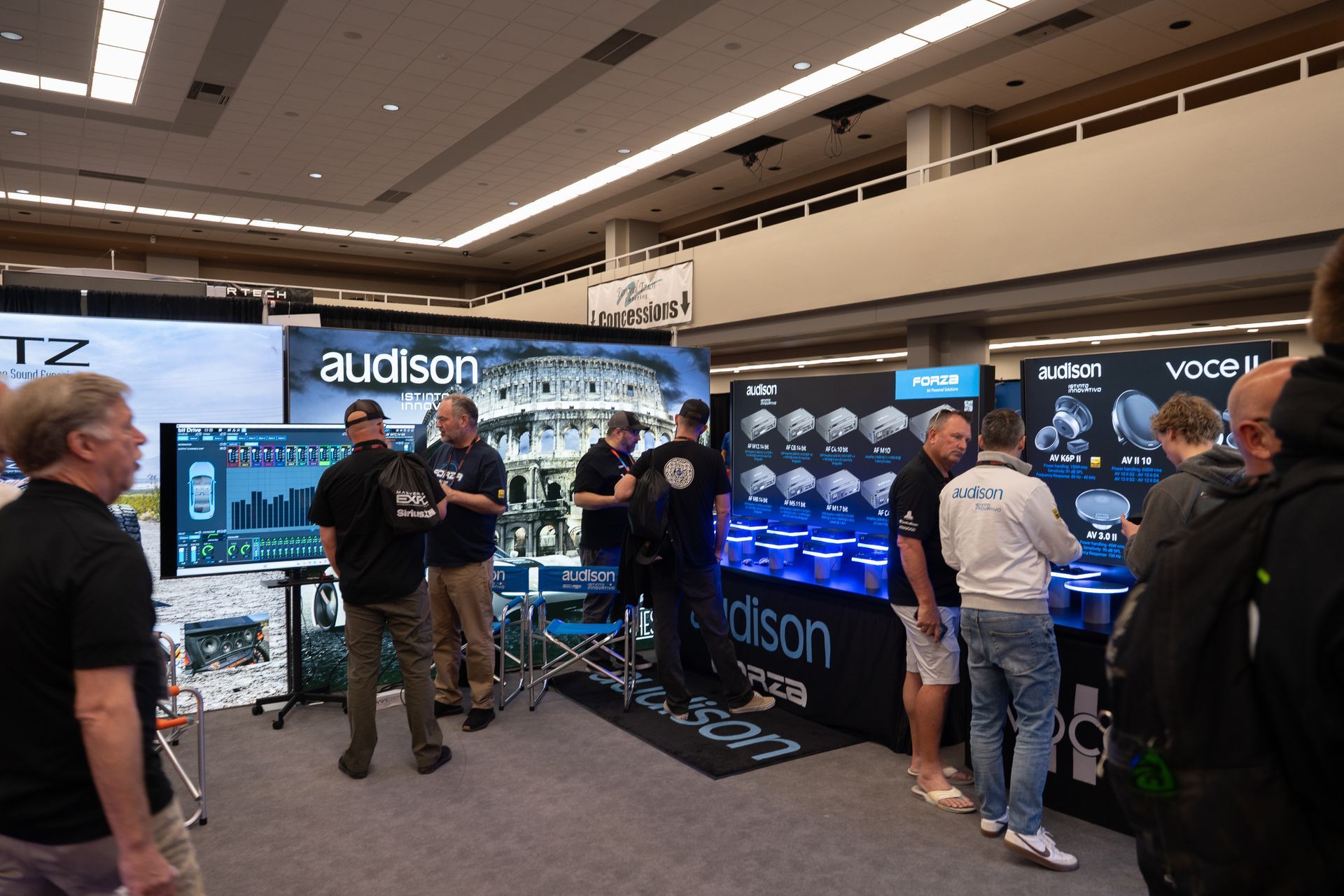 Audison booth at a trade show; people looking at products, some with employees.