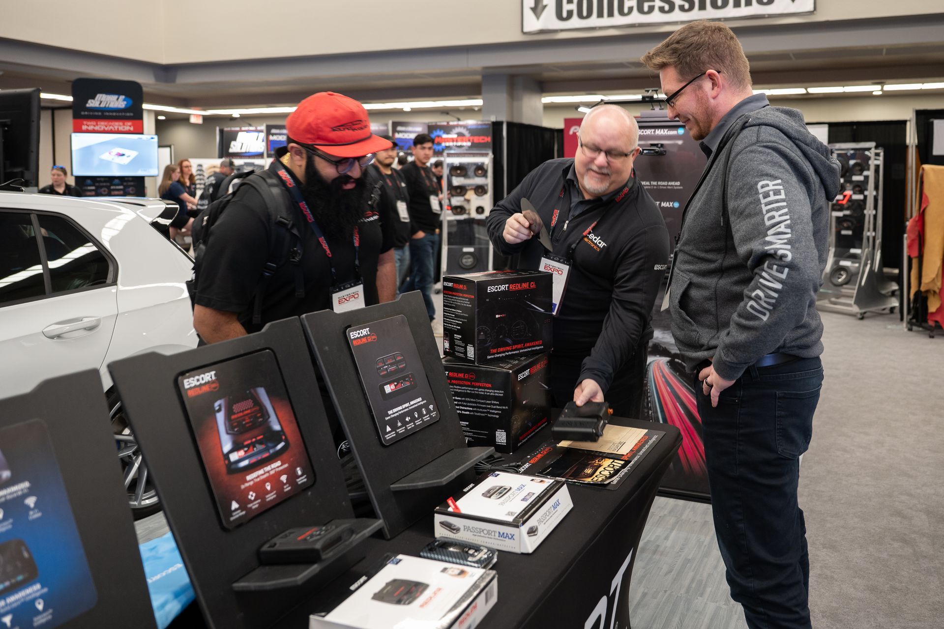 People at a booth, viewing and discussing car audio equipment at a trade show.
