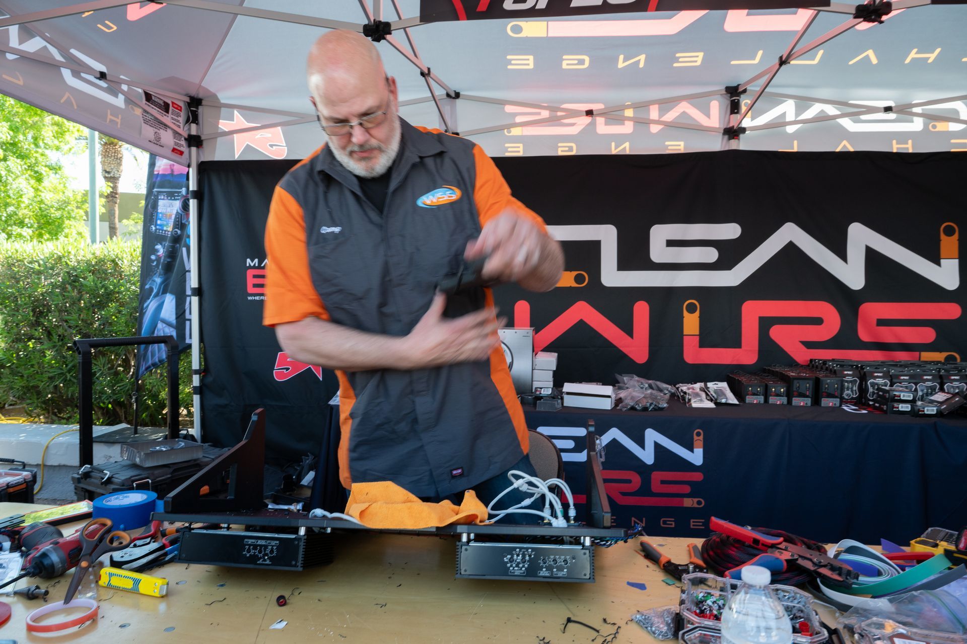 Man in orange vest assembling a device at a table, under a tent with “Clean Watts” branding.